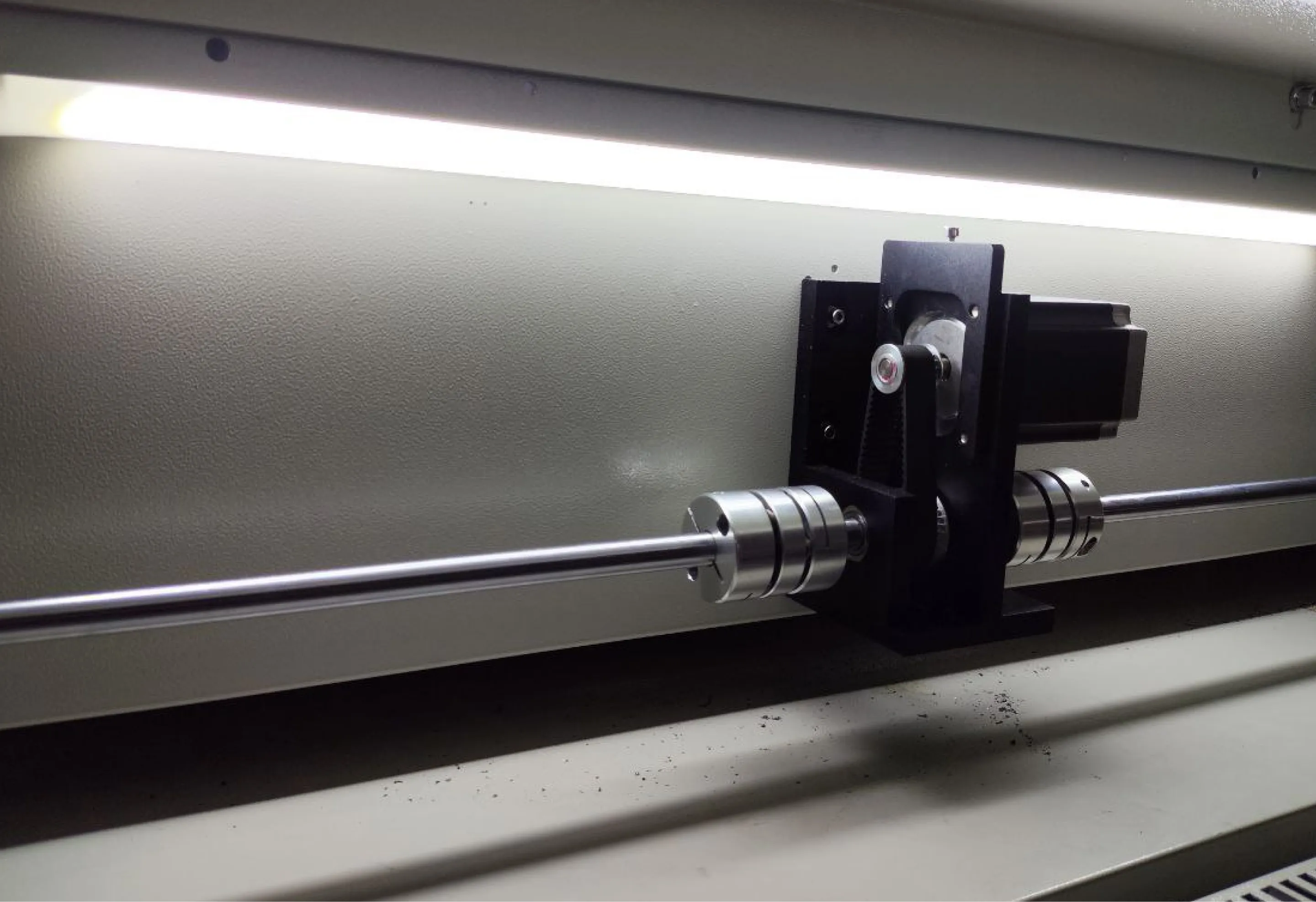 Узел станка: двигатель с ременной передачей, приводной вал и две гибкие муфты на фоне корпуса.