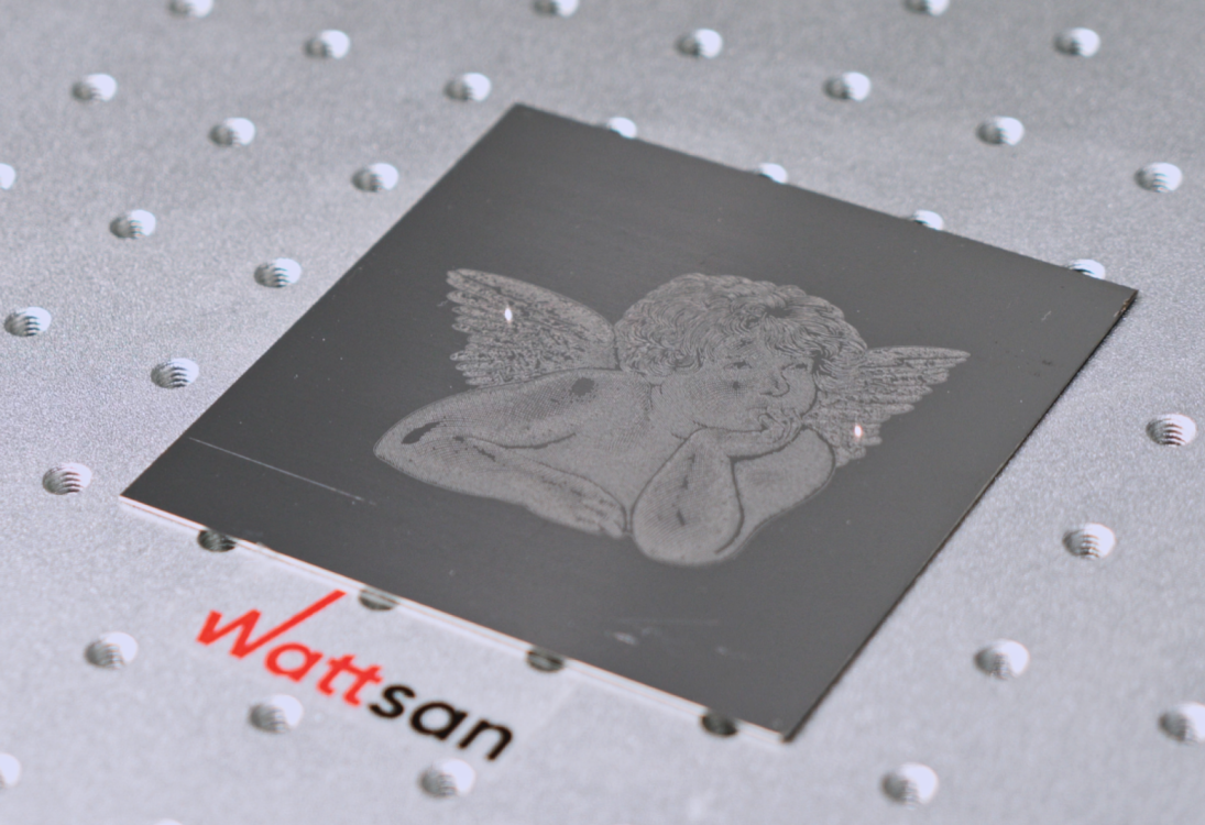Маленький чёрный квадрат с гравированным ангелом-херувимом, текст "Wattsan" ниже, на металлической точечной поверхности.